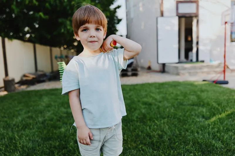 Playful boy holding an apple in the garden, enjoying a sunny day surrounded by greenery and a cheerful outdoor atmosphere, perfect for family memories.
