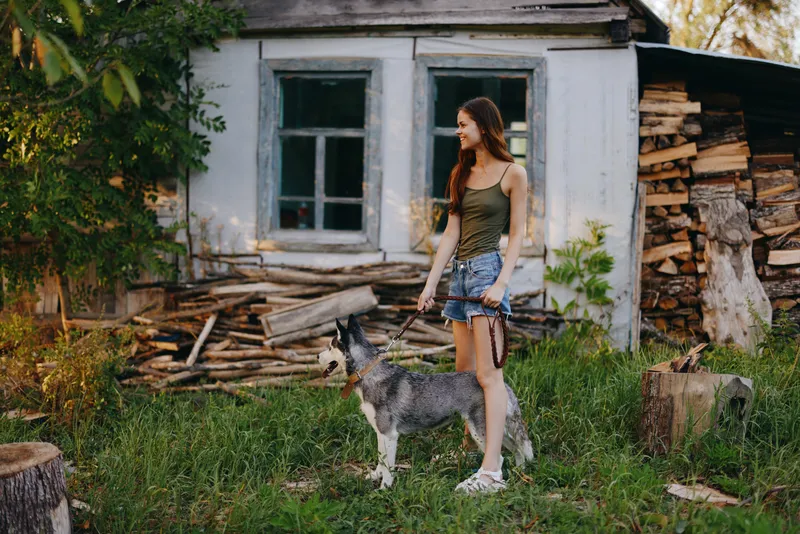 Женщина и её хаски весело играют на улице в парке среди деревьев, улыбаясь с зубами во время осенней прогулки со своим питомцем