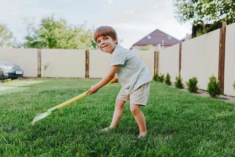 Happy boy playing in the garden with a rake, enjoying outdoor activities and the beauty of nature on a sunny day. Perfect for family and childhood themes.