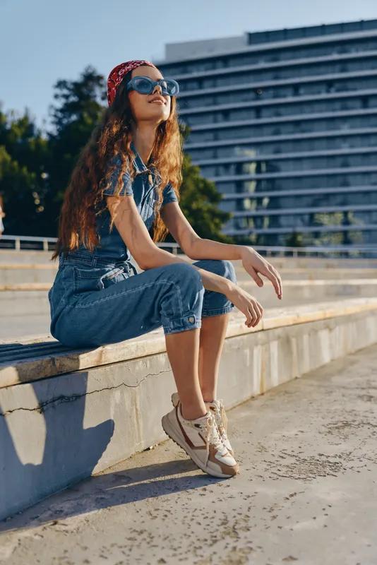 lifestyle woman in modern boho-western denim street style wearing casual sneakers and sunglasses, enjoying sunny urban outdoors with film color effect