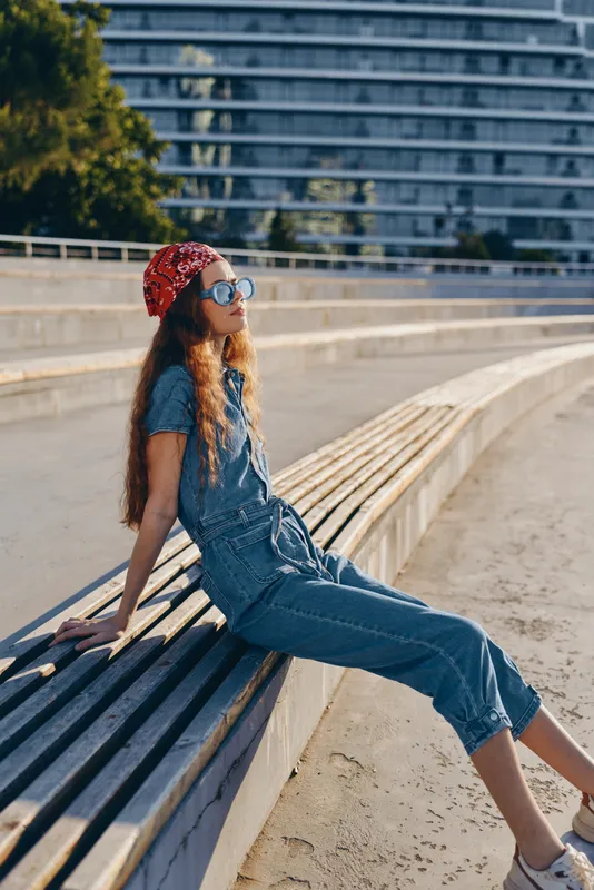 lifestyle woman in modern boho-western denim street style relaxing outdoors with film color effect and casual summer vibe on urban bench