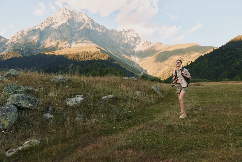 Young woman hiking in the mountains wearing shorts and backpack. Sunny day with clear sky and rocky peaks in the background. Concept of active lifestyle and adventure.