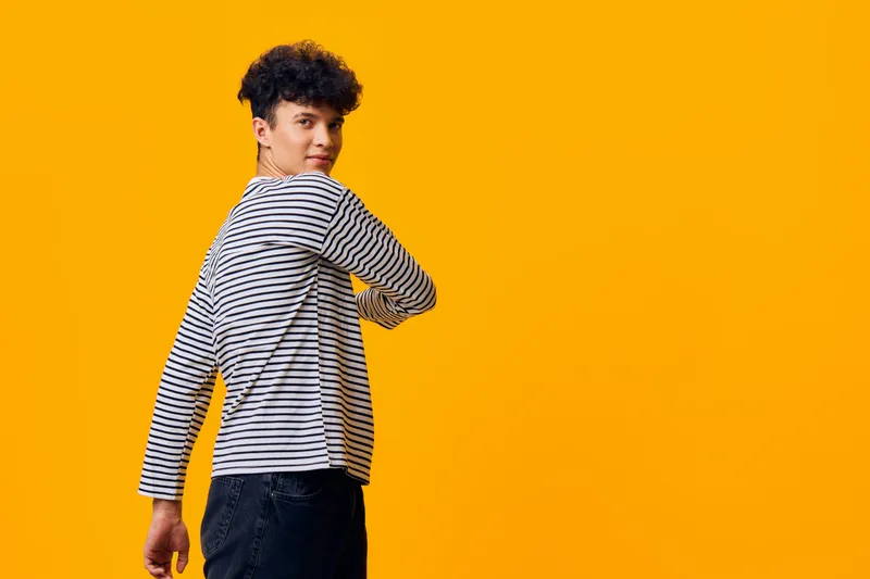 young man wearing striped shirt posing confidently against bright yellow background with casual style and curly hair, showcasing modern fashion and vibrant mood