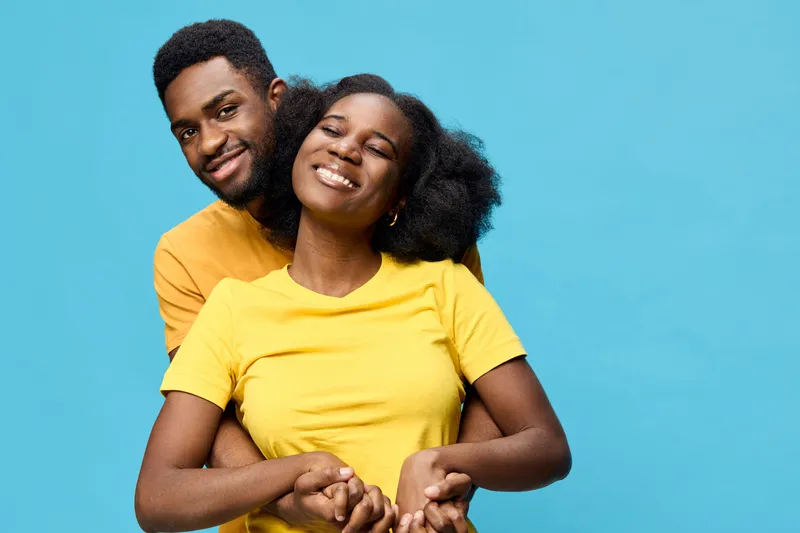 Young couple embracing with joy against a vibrant blue background, wearing matching yellow shirts, expressing love and happiness in a cheerful setting