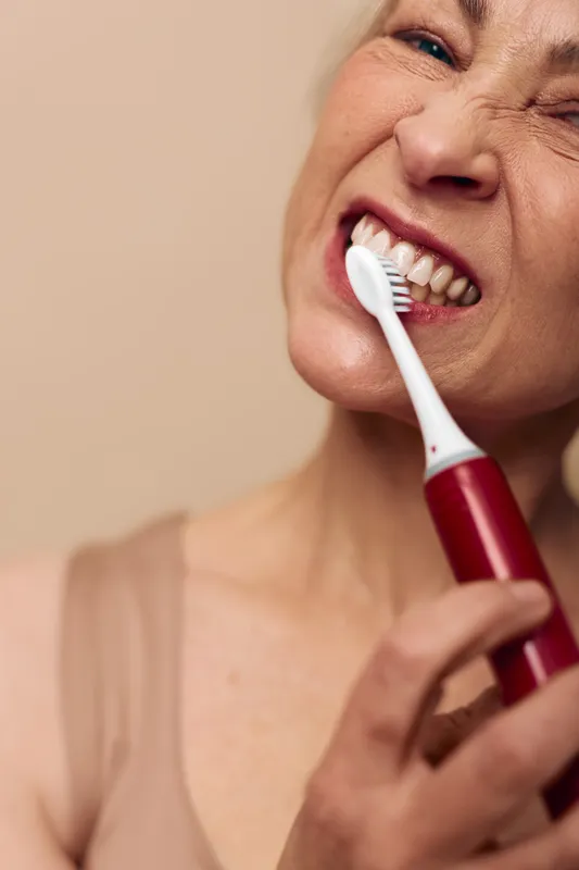 Close-up of mature woman brushing teeth with electric toothbrush, showing detailed oral care routine and dental hygiene concept for healthy lifestyle and personal wellness.