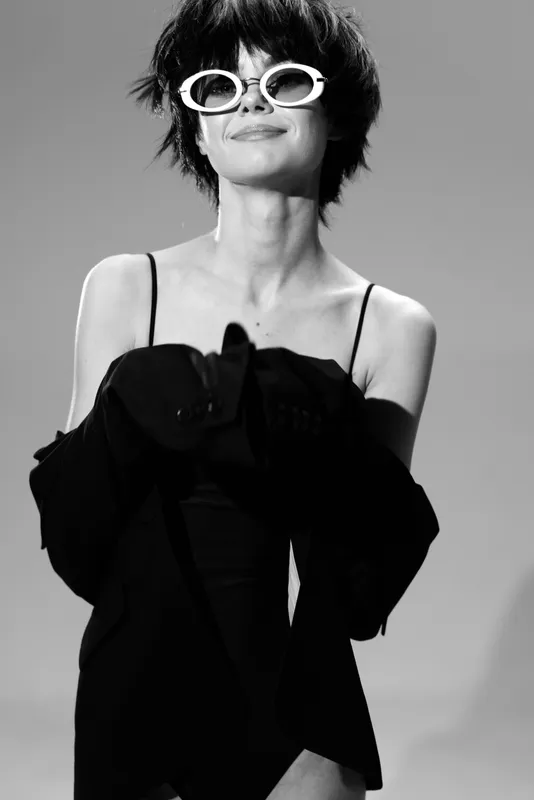 Black and white smiling woman with sunglasses wearing fashionable black dress and jacket, modern style, joyful emotion.