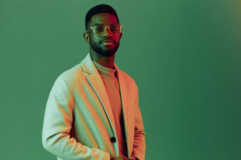 Stylish male model in a light gray blazer and glasses against a green background, embodying confidence and elegance