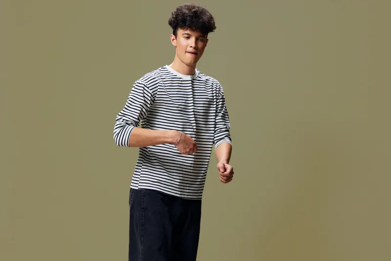 young man in striped shirt dancing joyfully against plain background with curly hair and casual black pants, expressing happiness and movement in studio setting