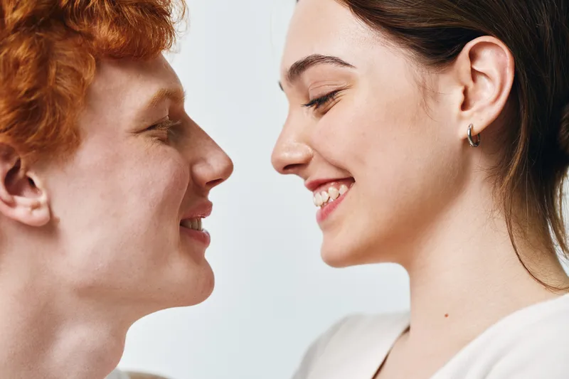 Young couple, man and woman smiling with close faces and closed eyes for love, relationship and happiness on white background in studio. Intimacy, affection, and joy.