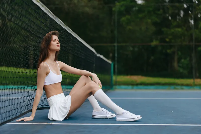 Young female athlete in sporty attire enjoying a moment of relaxation on a tennis court, embodying a healthy lifestyle and confidence