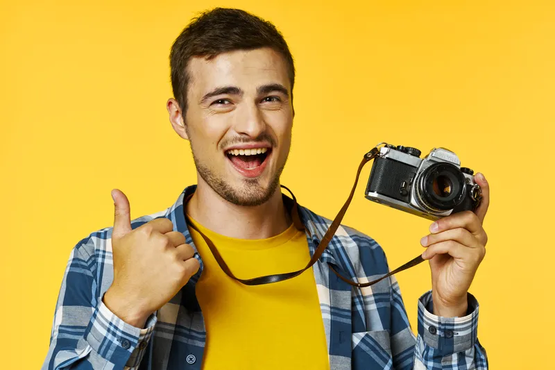 Успешный фотограф с камерой показывает большой палец и смеётся в камеру
