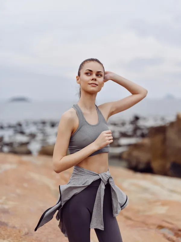 Young woman in activewear in a coastal setting, exuding confidence and vitality, representing a healthy lifestyle and fitness concepts, gray tones and natural scenery