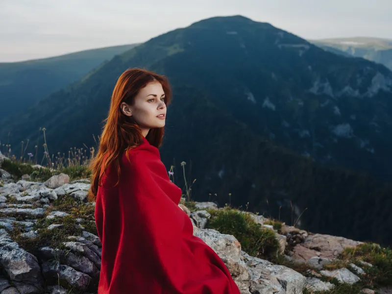 Женщина в горах прячется под пледом