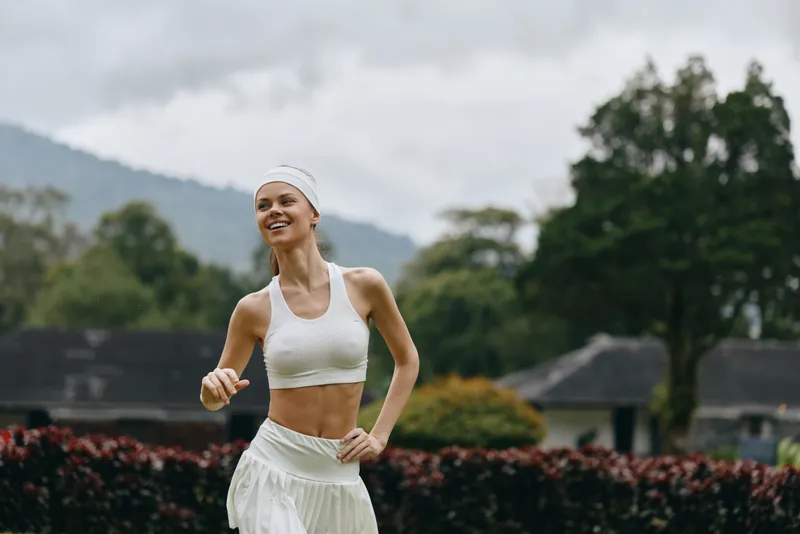 Young athletic woman jogging outdoors in a natural setting, wearing a white sports outfit and a headband, radiating happiness and vitality