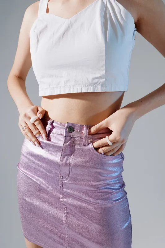 Close-up of a woman wearing a white crop top and a shiny pink skirt. The image focuses on fashion and beauty with a modern and stylish concept.