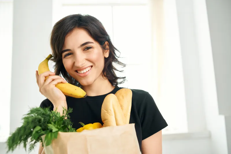 Жизнерадостная женщина с пакетом продуктов на кухне