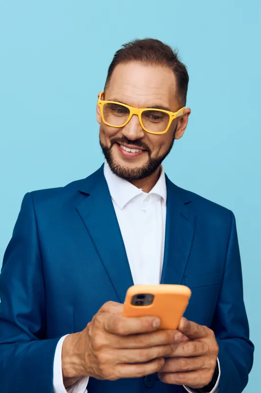 A professional man on a colored isolated backdrop exudes confidence and focus while using a smartphone, a modern business portrait showcasing motivation and calm leadership.