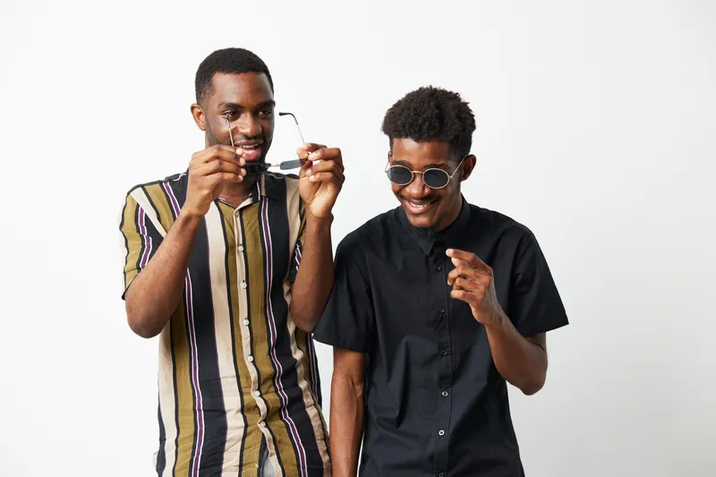 Two joyful African American men wearing stylish sunglasses, captured in a lively moment together, showcasing friendship, laughter, and playful interaction.