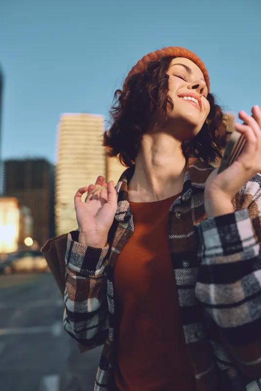 woman portrait smile city candid authenticity lifestyle golden hour: young woman in beret and plaid coat enjoying golden hour glow, candid lifestyle moment of mindful living and emotional