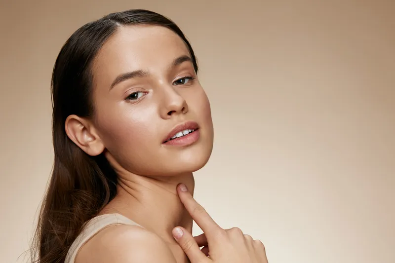 Young woman with natural beauty and a gentle expression, showcasing healthy skin and minimal makeup against a soft beige background