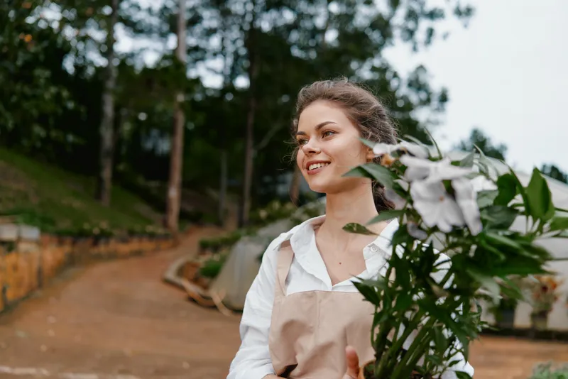 Young woman with floral bouquet in apron, smiling outdoors in a garden setting, showcasing a joyful connection with nature during spring season