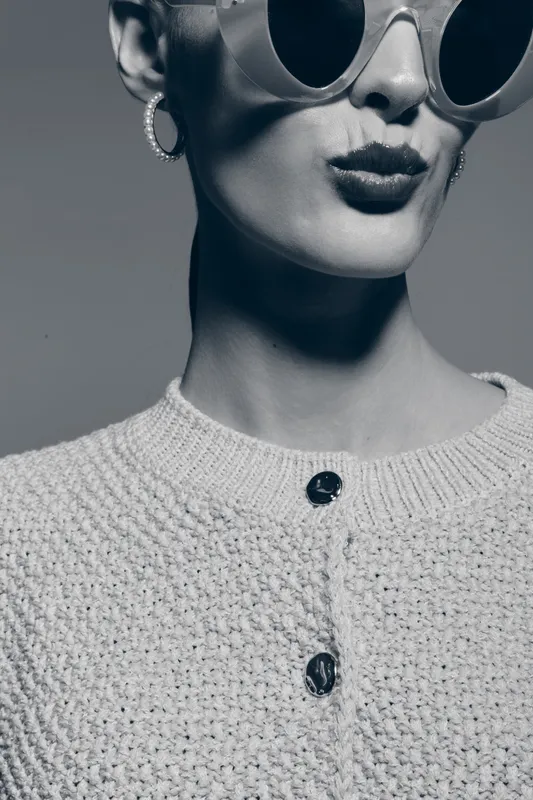 Stylish caucasian woman with pale skin wearing round sunglasses and hoop earrings in monochrome close-up portrait.