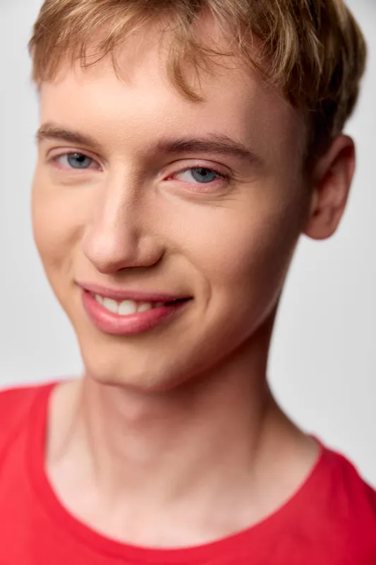Closeup of a smiling young man with blond hair in a red shirt, warm lighting and clear skin, ideal for lifestyle, youth, and positive image campaigns