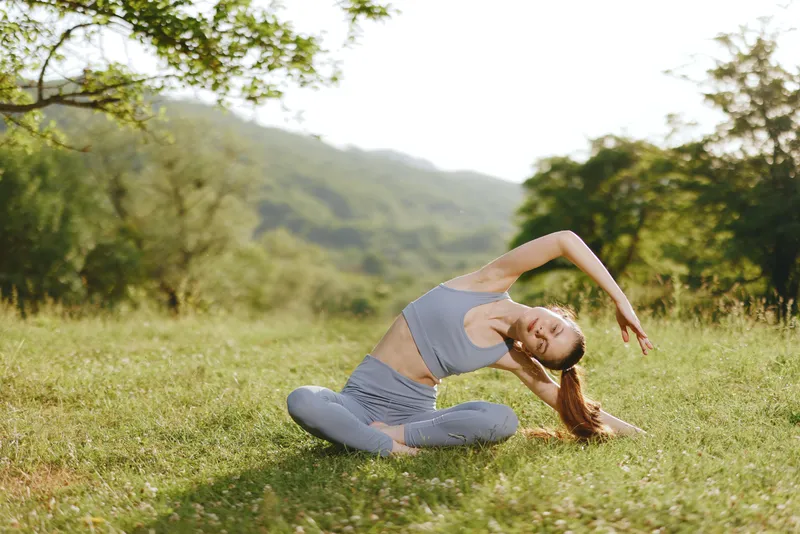 Young woman practicing yoga in a serene outdoor setting, wearing comfortable athletic wear, expressing tranquility and balance in a lush green environment