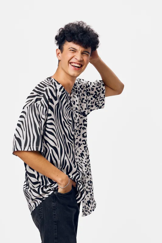 smiling man in zebra print shirt laughing happily with hand behind head, casual black jeans, curly hair, isolated white background, youth lifestyle portrait