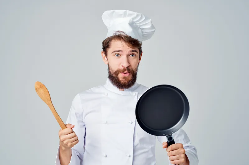 Повар готовит с использованием кухонной утвари, включая сковороду, в ресторане