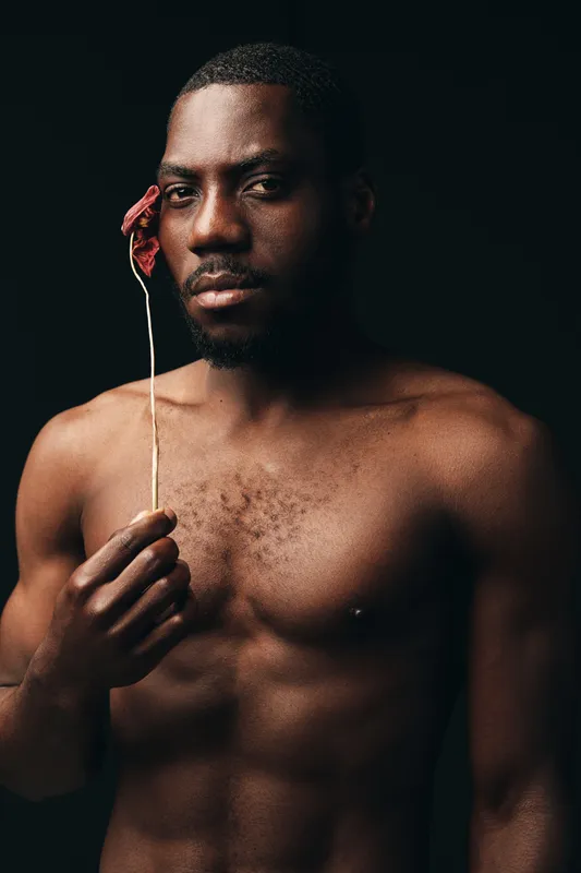 African man with dark skin holding dried flower in creative conceptual visual style, portrait with serious expression and artistic mood on black background for modern art.