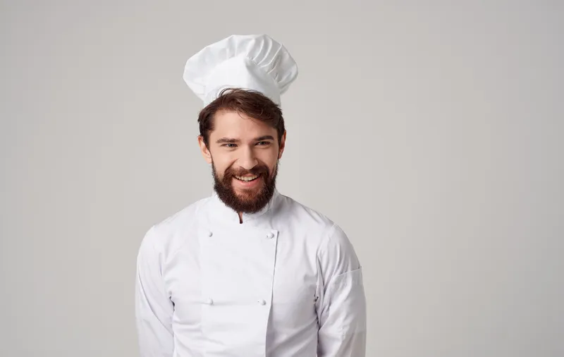 Мужчина в форме повара, занимающийся кулинарией, демонстрирует эмоции гурмана, позируя в студии