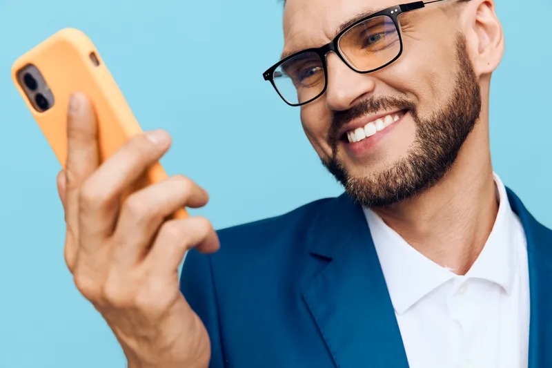 A confident business professional smiles while taking a selfie against a bright colored background, presenting a modern, isolated portrait of success and tech savvy.