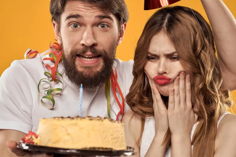 Бородатый мужчина с тортом и скучающая девушка на празднике