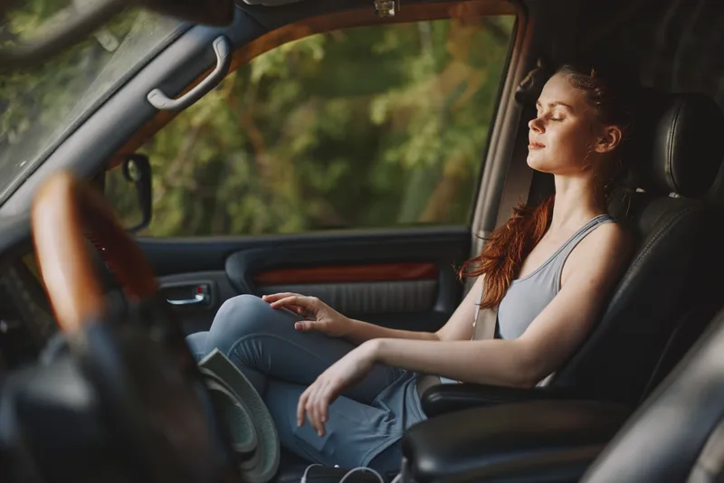 Young woman relaxing in car with eyes closed, enjoying calm moment in nature, wearing casual attire Emphasizing tranquility, serenity, and connection to the outdoors