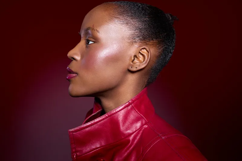 Profile of a dark skinned African woman with shiny skin wearing a red leather jacket against a red background. Concept of beauty, fashion, and confident female model portrait.
