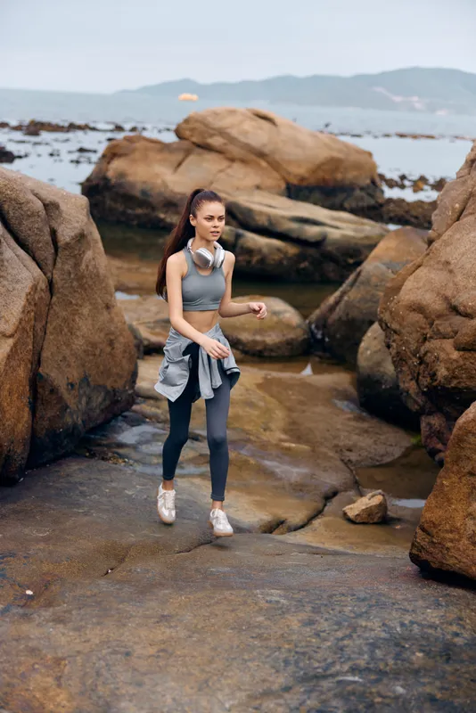 Young woman exercising outdoors on rocky beach promoting fitness and healthy lifestyle with a scenic natural background and activewear in cool tones
