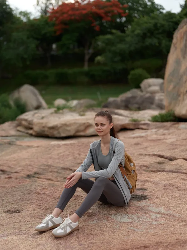 Young female model in activewear sitting on a rock, expressing serenity surrounded by nature, ideal for healthy lifestyle themes, outdoor activities, and fitness motivation