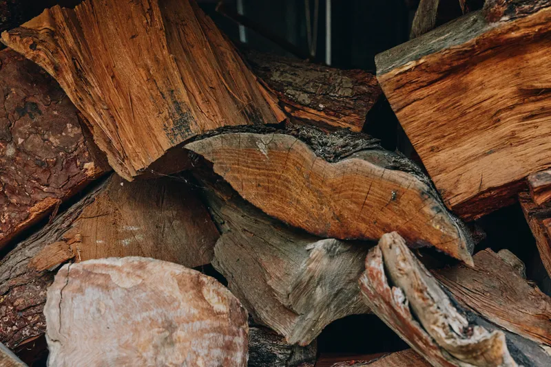 Firewood and split logs in a stacked woodpile of seasoned hardwood and timber, kindling pieces visible with rich bark texture closeup, cozy rustic fuel supply for fireplace.