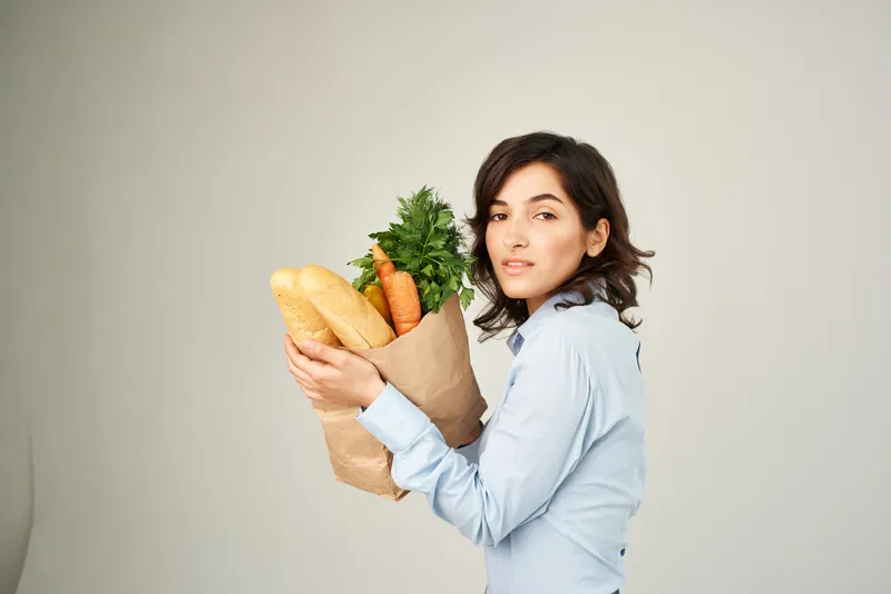Веселая женщина с пакетом продуктов из супермаркета покупает овощи