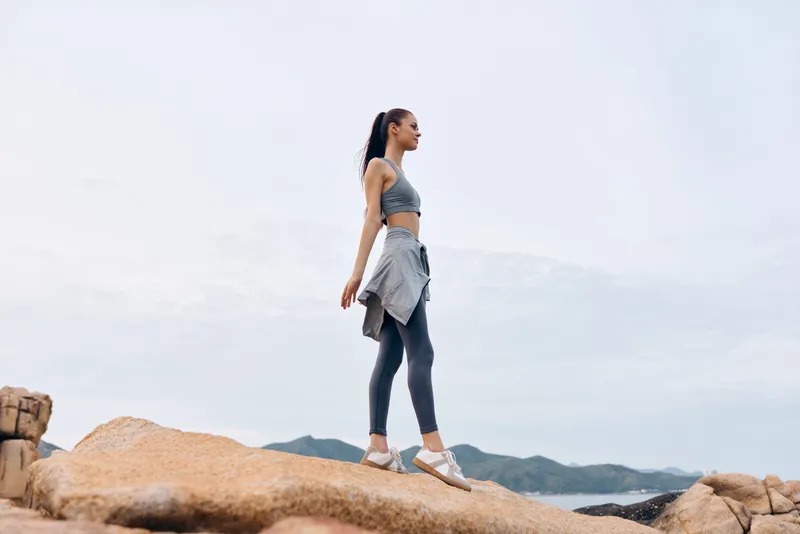 Fit young woman in activewear confidently walking on rocky terrain, showcasing determination, strength, and the beauty of nature in a serene landscape