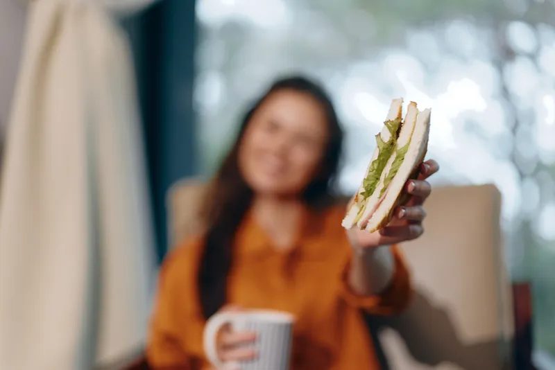 Весёлая молодая женщина наслаждается вкусным полезным сэндвичем, демонстрируя сбалансированное питание в спокойной обстановке в помещении