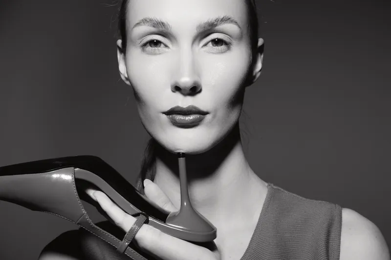 Portrait of a white woman with pale skin holding a high heel shoe, looking confident in black and white studio lighting.