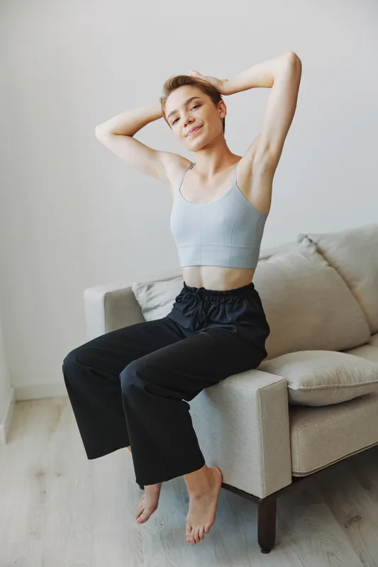 Девушка-подросток сидит на диване дома, улыбается в домашней одежде и очках, с короткой стрижкой