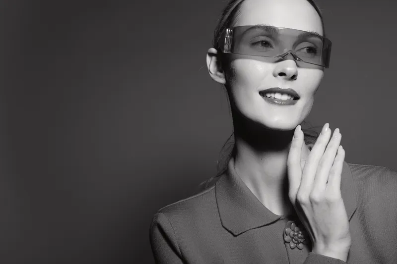 Slavic woman with light skin and brown hair smiling and wearing transparent glasses and textured jacket. Studio portrait in black and white with elegant mood and fashion concept.