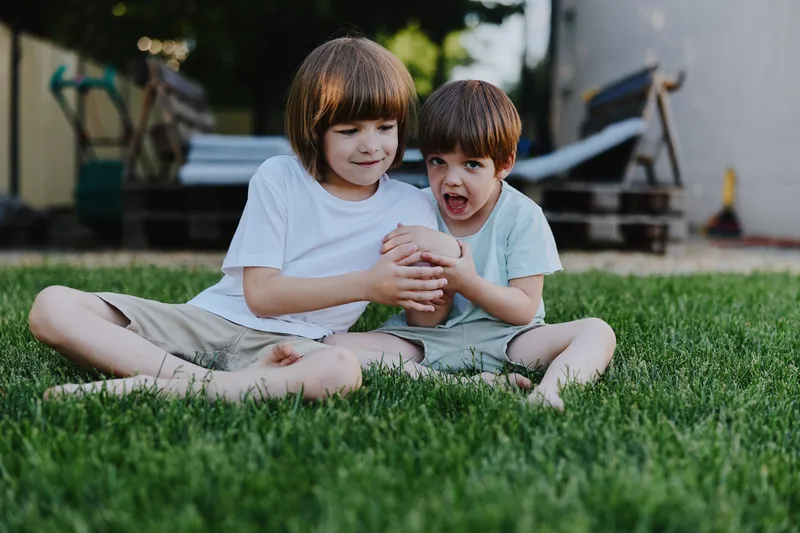 Happy children sitting on the grass, enjoying their playful moment. Two joyful boys holding a ball, creating a carefree and vibrant atmosphere outdoors.