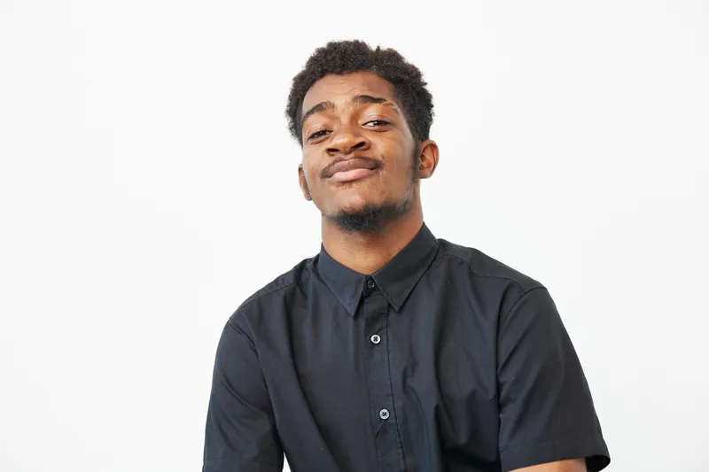Confident black man with a charming smile against a light backdrop, showcasing his style and attitude. Ideal for representing diversity and self-expression in visuals.