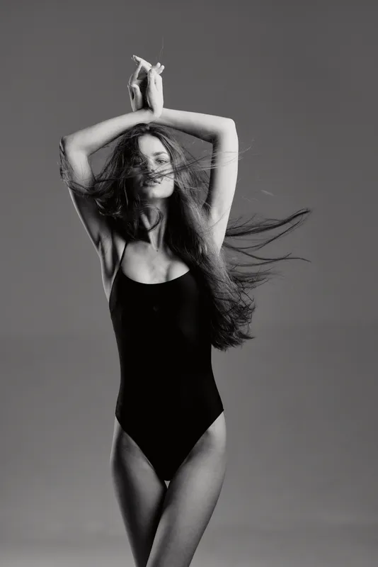 Black and white portrait of a young woman dancing with flowing hair and expressive pose in studio lighting.