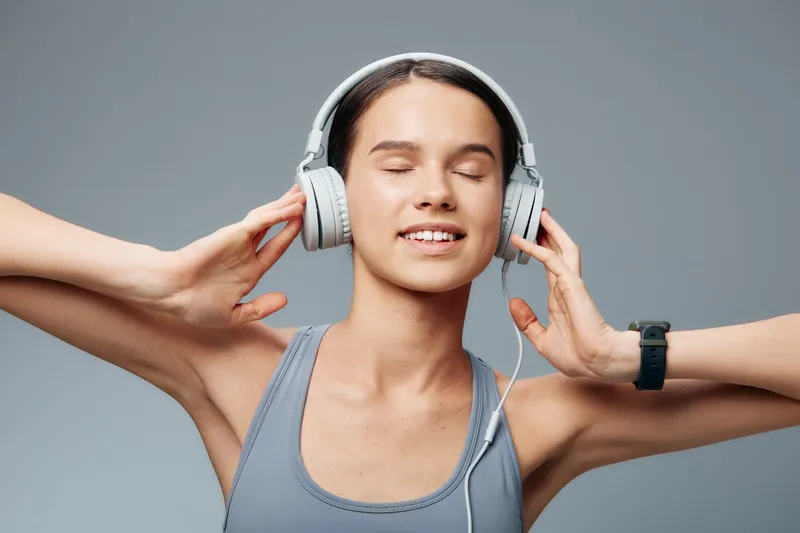 Woman fitness enthusiast wearing headphones, enjoying music during workout in a studio. Relaxed pose with eyes closed, athletic tank top, calm energy and focus.