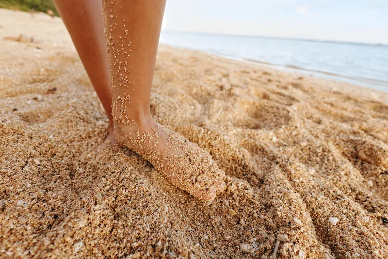 Close-up of a barefoot foot sinking into warm beach sand under bright sun, capturing relaxation, outdoor leisure, and the simple joy of a seaside moment.
